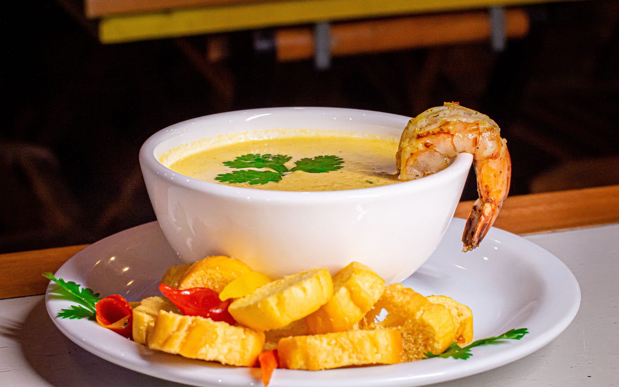Tigela de sopa cremosa de camarão decorada com coentro e fatias de pão no prato