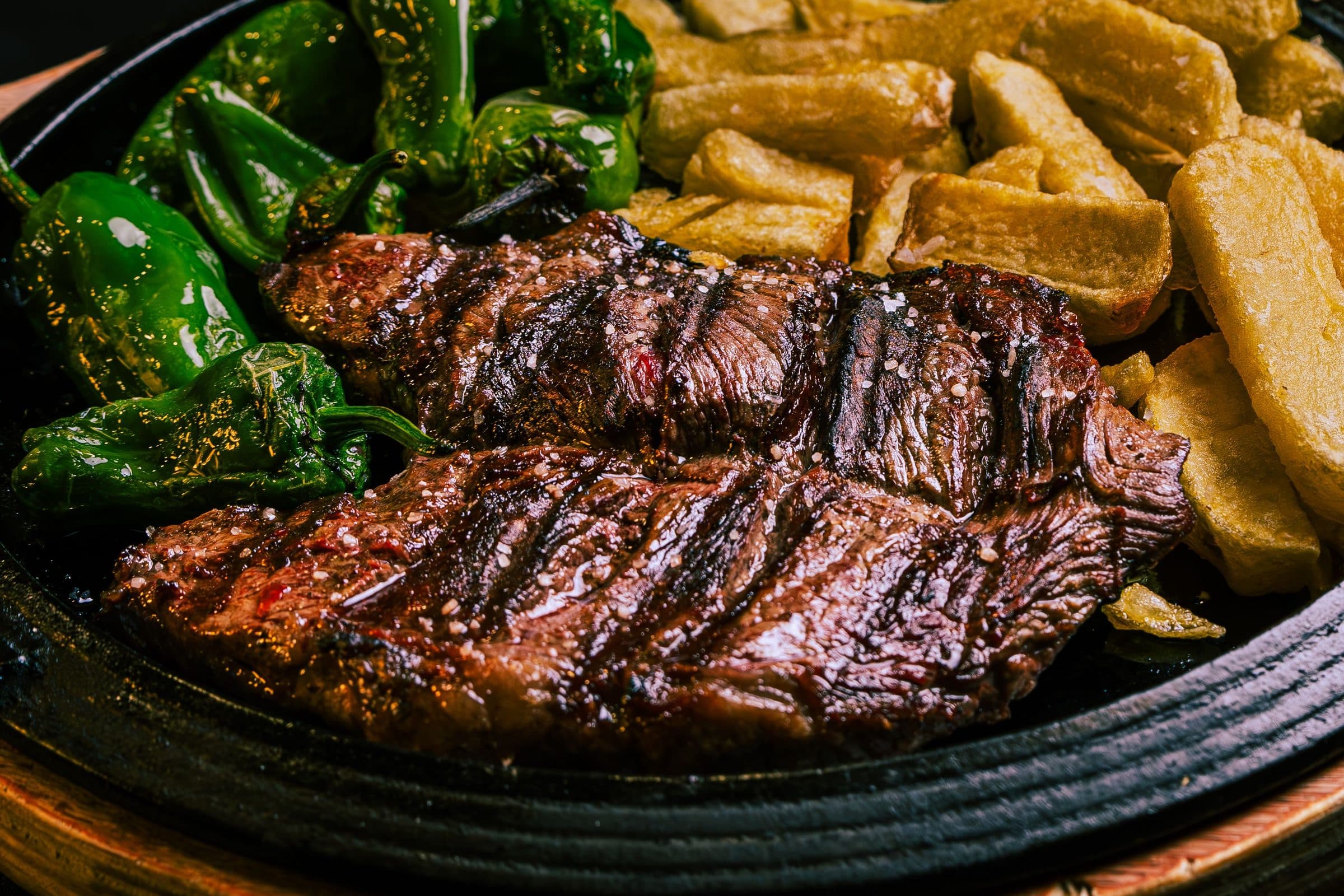 Bife bovino grelhado servido em um prato com pimentões verdes e batatas crocantes