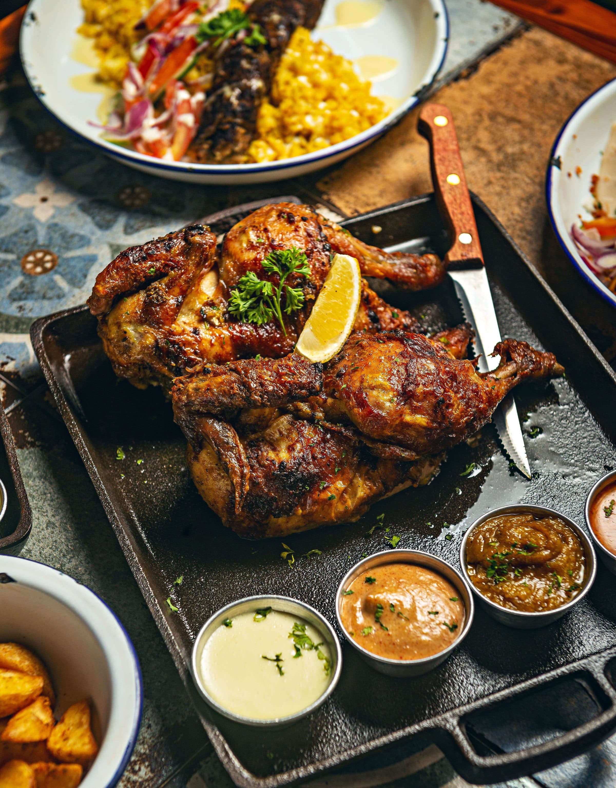Frango grelhado servido com molhos e acompanhamentos em uma travessa rústica