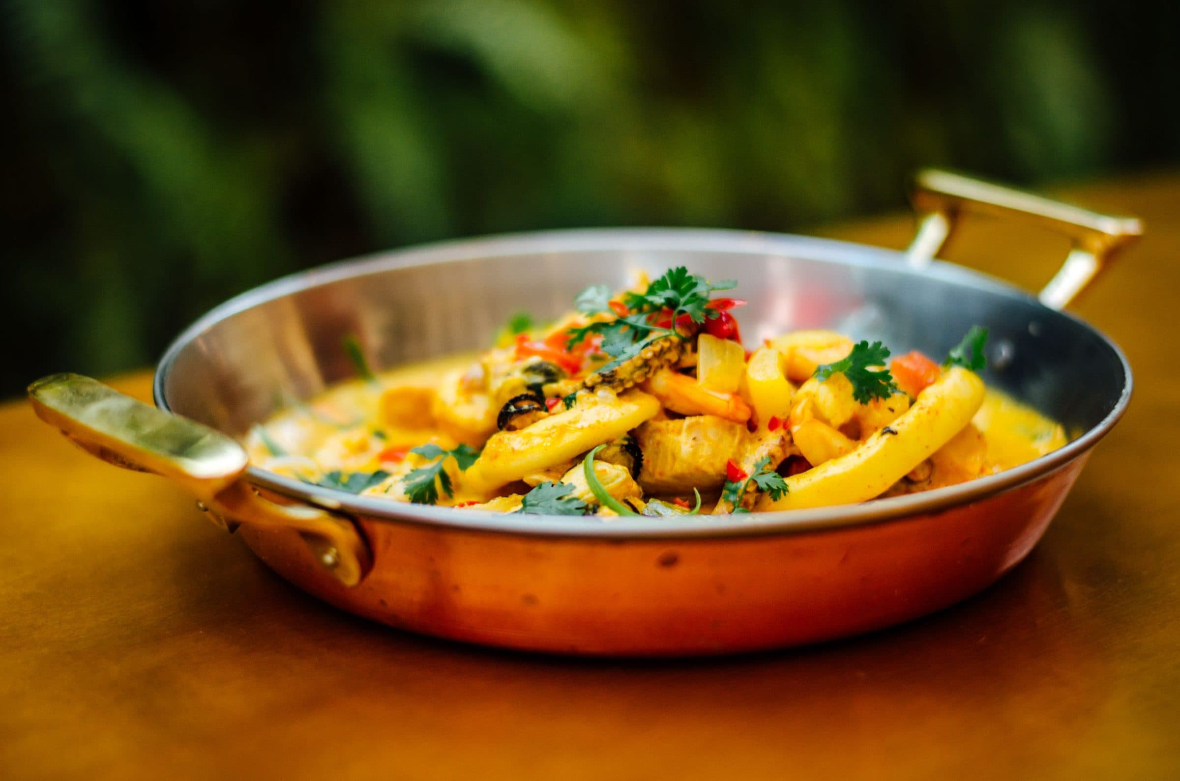 Massa com frutos do mar servida em uma panela de cobre com ingredientes coloridos