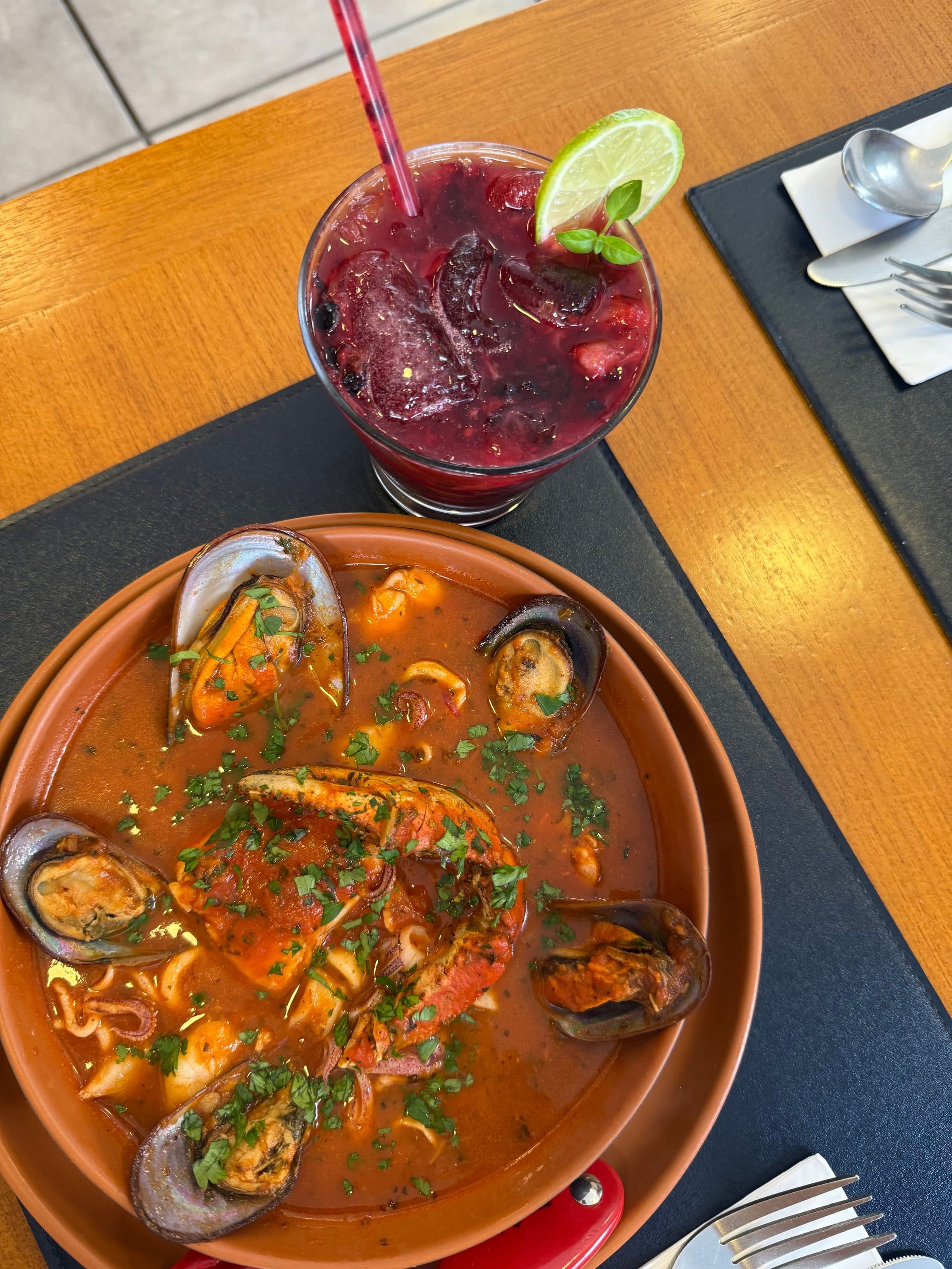 Ensopado de frutos do mar com camarões e mexilhões ao lado de um drinque de frutas vermelhas